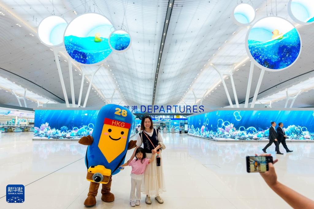 5月27日，旅客在香港国际机场二号客运大楼离境大堂与机场吉祥物合影。新华社记者 朱炜 摄